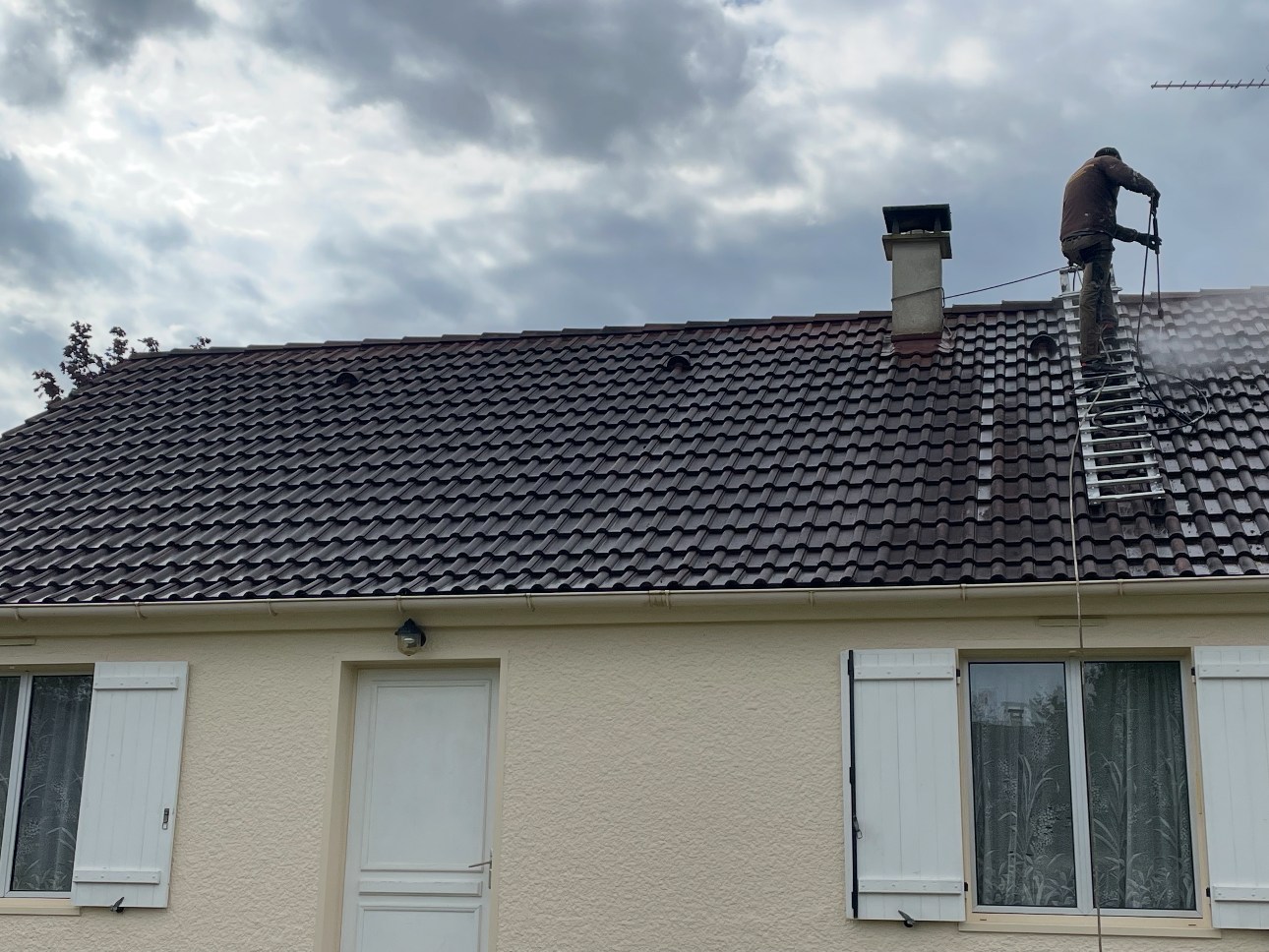 Couvreur en hauteur nettoyant une toiture au nettoyeur haute pression
