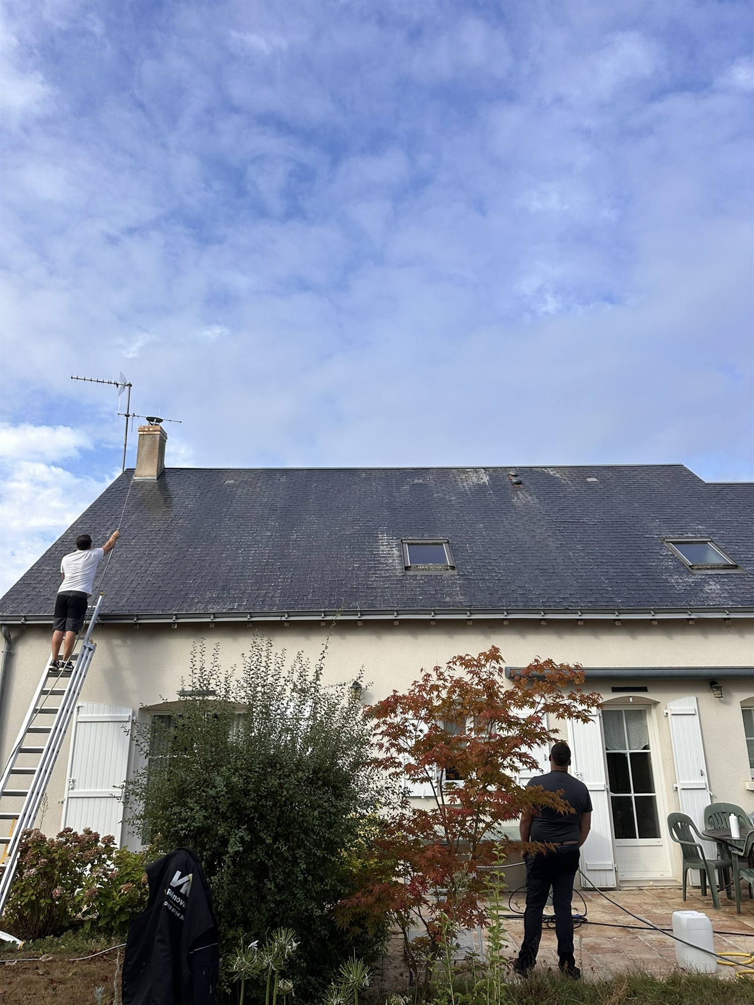 Couvreur sur une échelle nettoyant une toiture en ardoise
