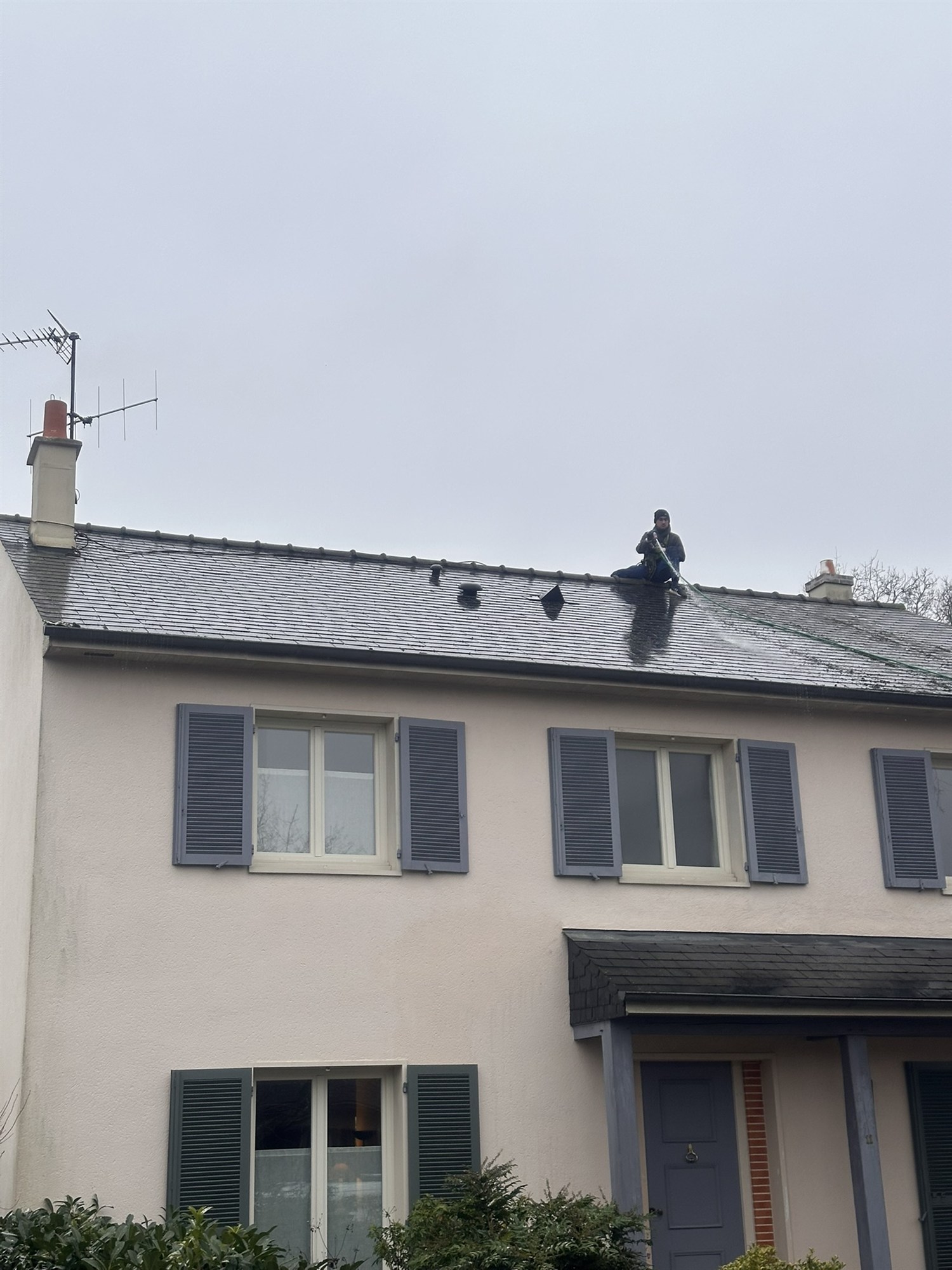 Couvreur assis sur le faîtage d'un toit pendant un nettoyage