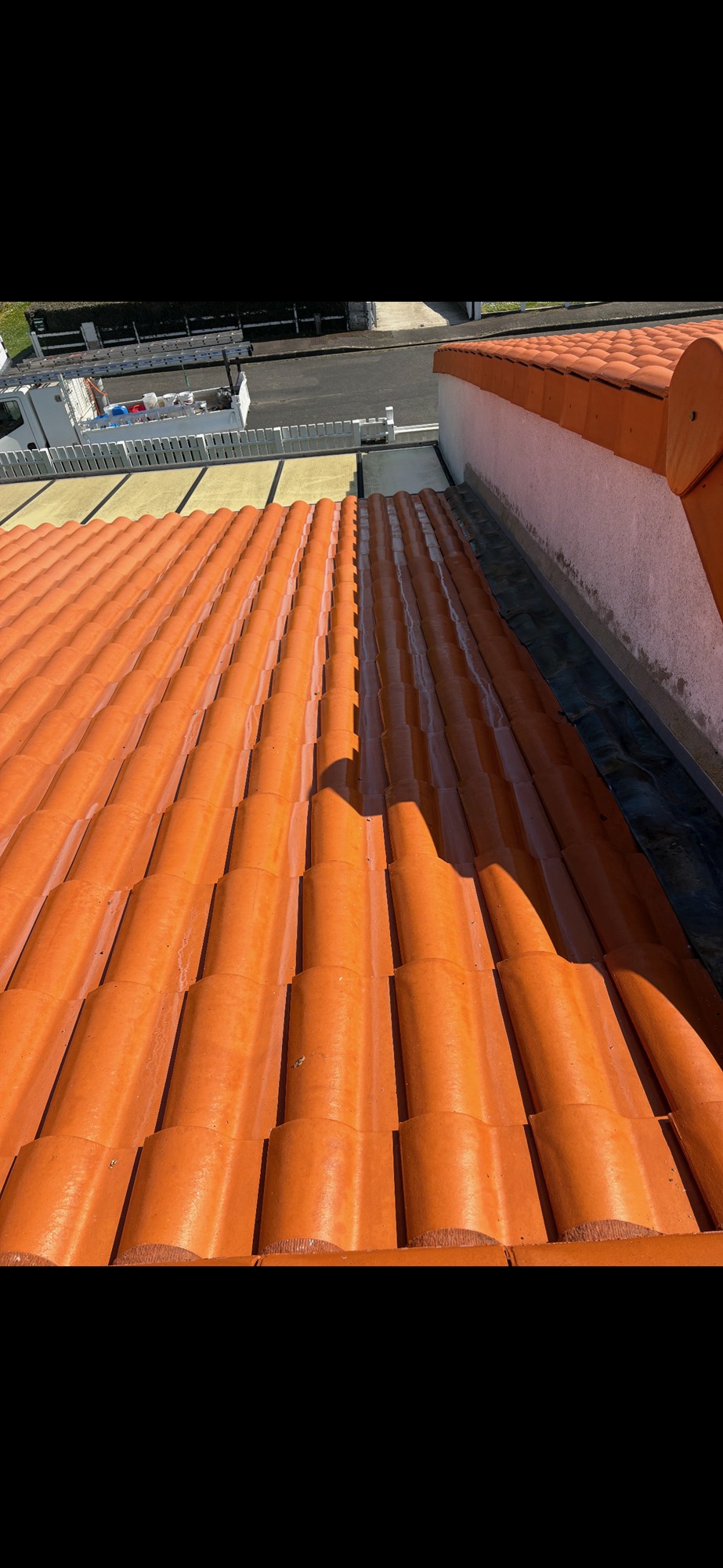 Toiture en tuiles photographiée en plein nettoyage : moitié encore sombre et couverte de lichen, moitié déjà nettoyée et orange vif